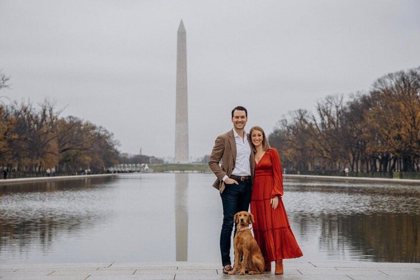 A couple standing by a body of water with a tall monument in the background. 1