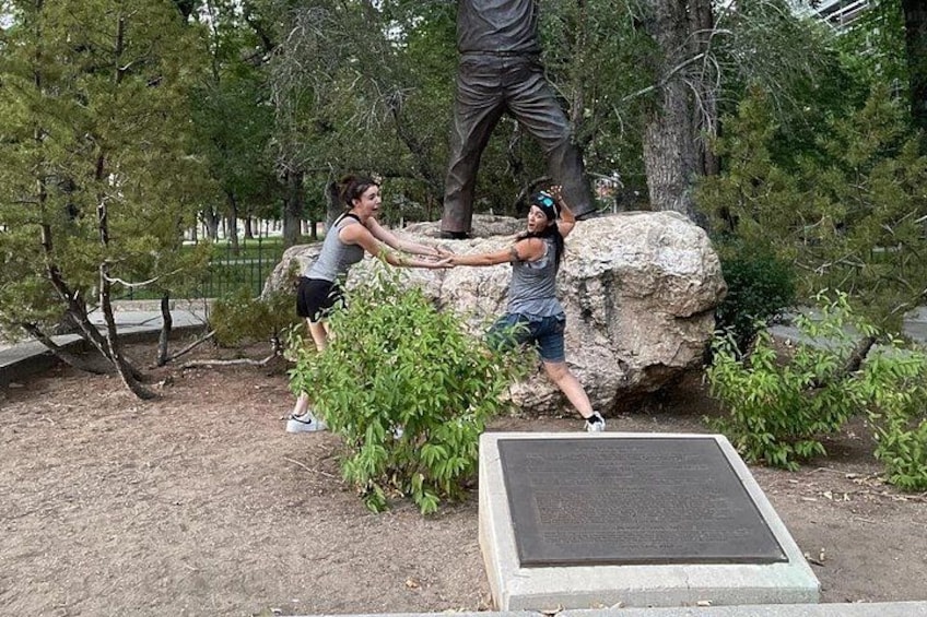 Two people climbing a rock formation in a park with trees and a monument in the background. 1
