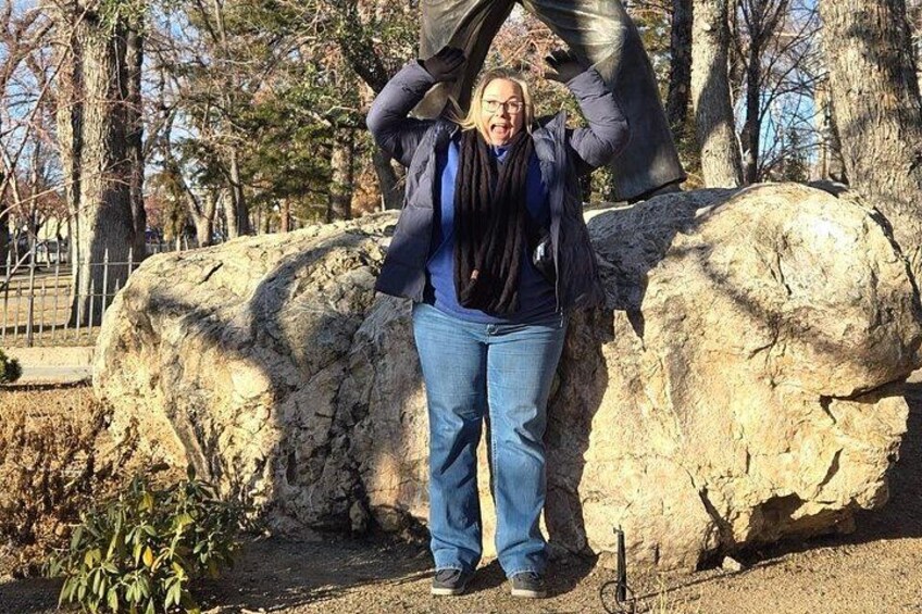 A person standing next to a large rock in a park with trees in the background. 2