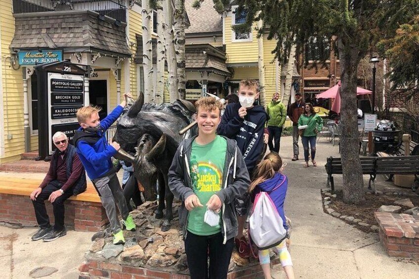 A group of people in front of a bull statue, with buildings and a signboard in the background. 2