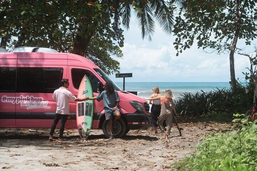 A pink bus parked on a beach with people around it. 2
