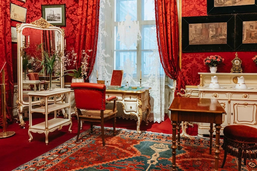 A richly decorated room with red walls, ornate furniture, and a large mirror. 5