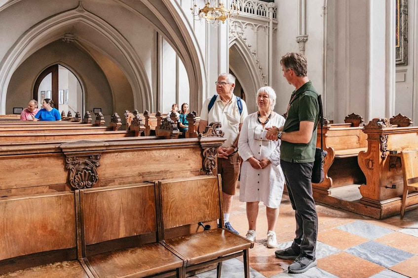 A church interior with wooden pews and a high arched ceiling. 1