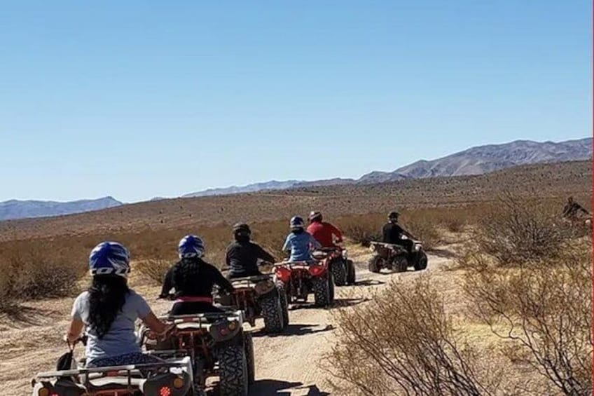 A group of people on ATVs on a dirt road in a desert landscape with mountains in the background. 5