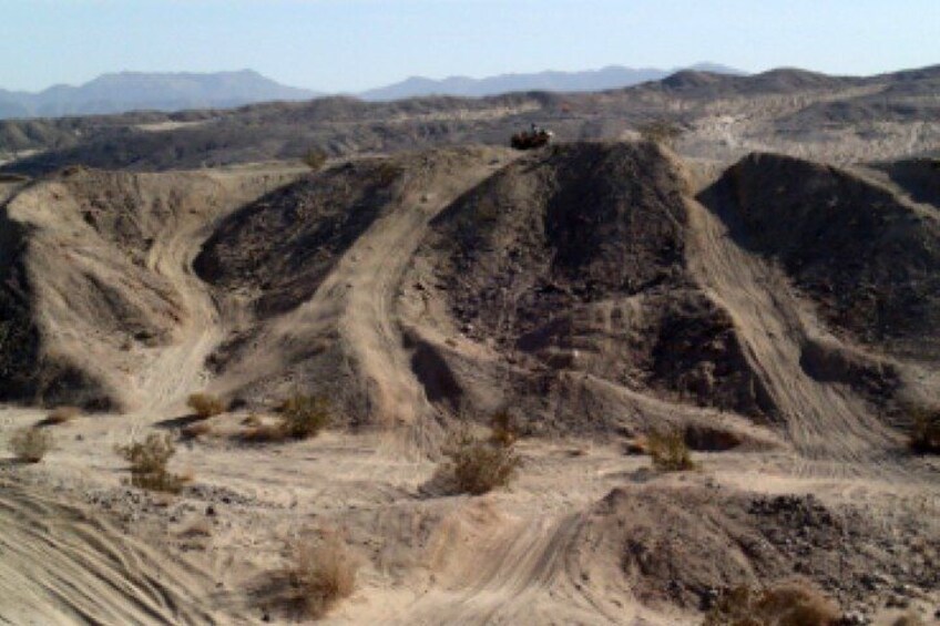 A rugged desert landscape with undulating hills and a dirt road. 2