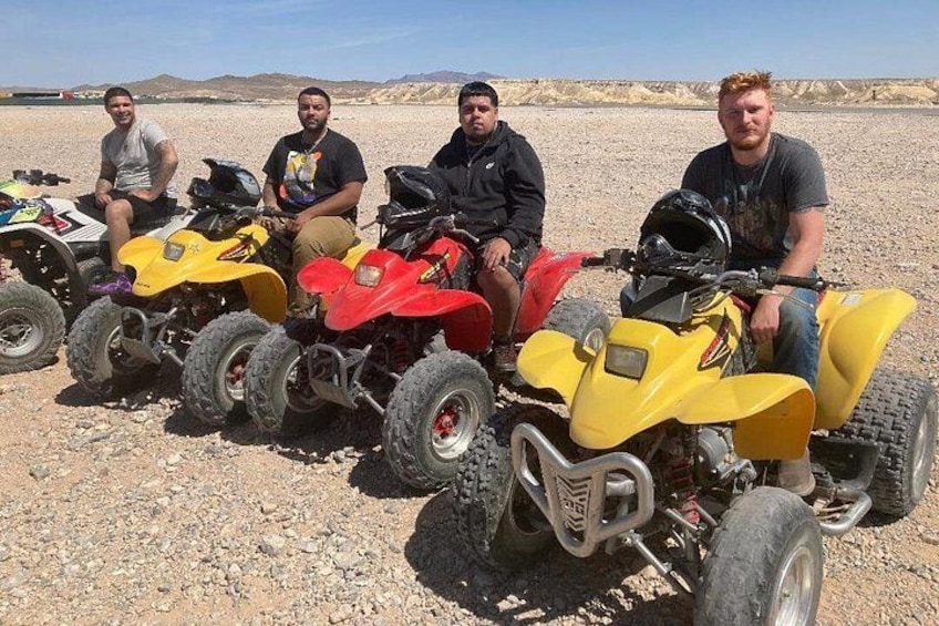 Vier personen zitten op quad bikes in een woestijn. 1
