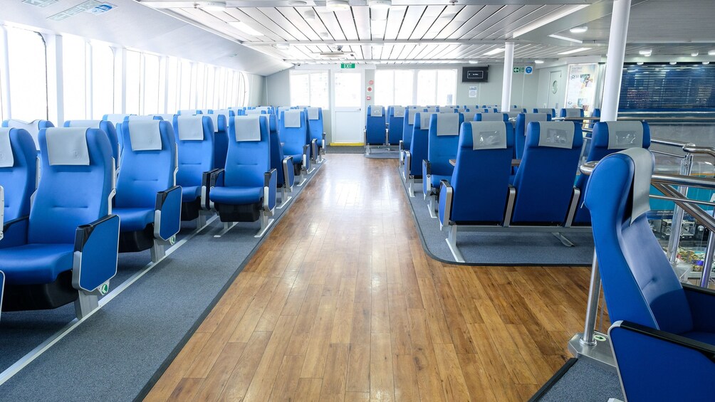 A clean, modern train carriage with rows of blue seats and wooden flooring. 2