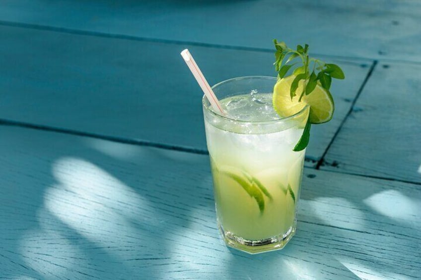 A glass of iced beverage with a lime wedge and mint garnish on a wooden surface. 3