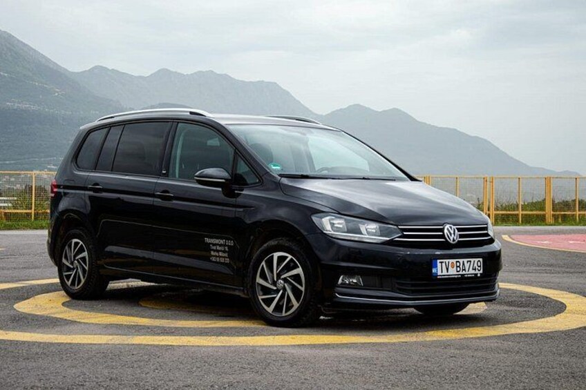 Een zwarte Volkswagen auto met een zichtbaar kenteken, geparkeerd op een weg met gele markeringen en bergen op de achtergrond. 2