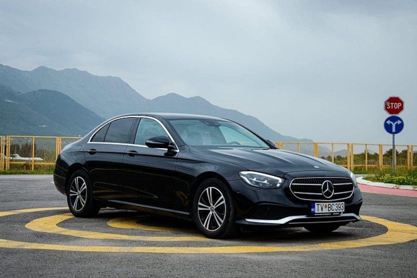 A black Mercedes-Benz car parked on a road with a stop sign and a roundabout sign in the background. 2