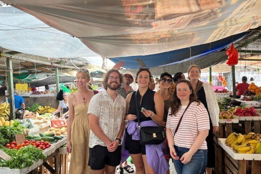 A group of people at an outdoor market with various fruits and vegetables on display. 2