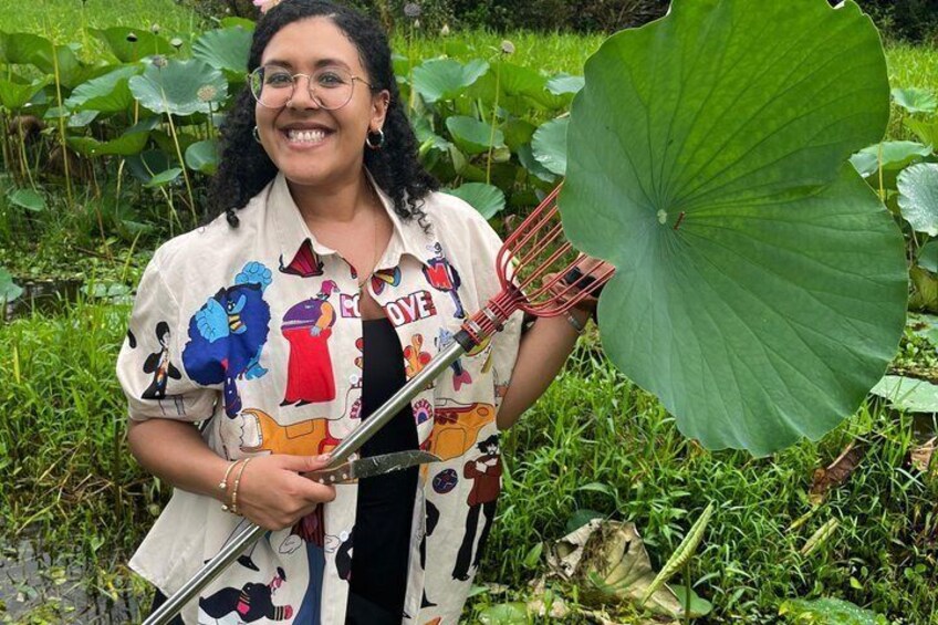 A person holding a rake in a garden with large green leaves and grass. 3