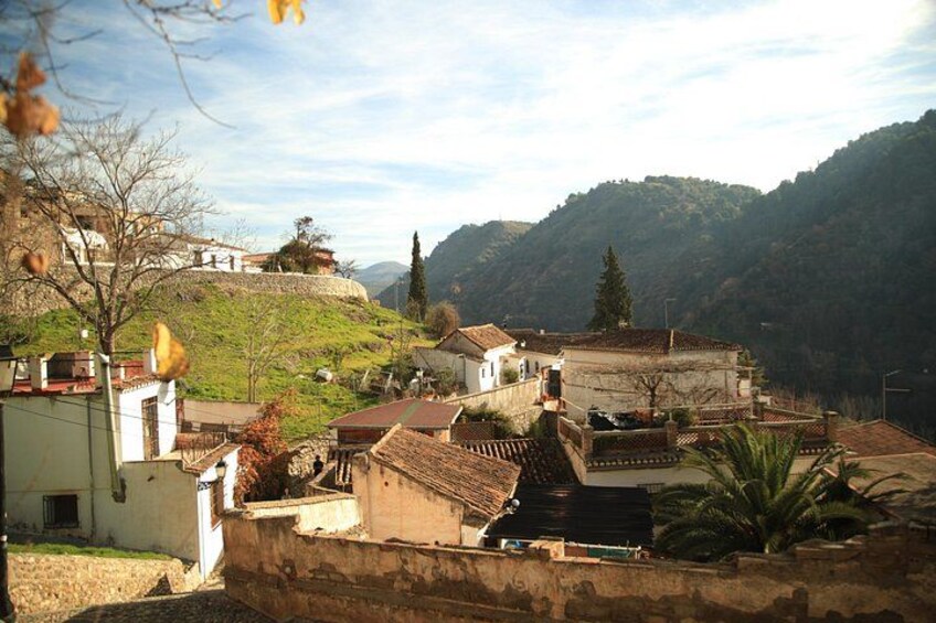Un pueblo en la ladera de una colina con edificios tradicionales, una iglesia destacada y una fortaleza en la cima. 3