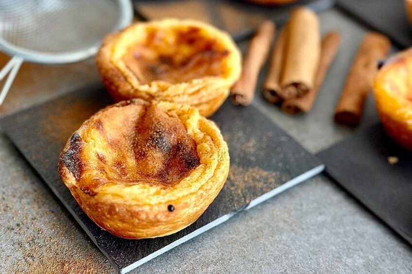Two Portuguese custard tarts on a dark plate with cinnamon sticks in the background. 4