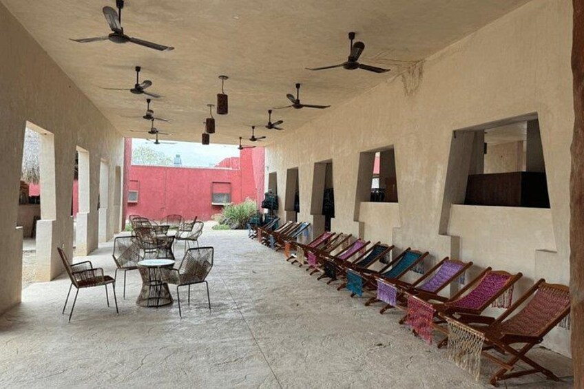 An outdoor covered area with ceiling fans, a row of colorful woven chairs, and a table with chairs. 5