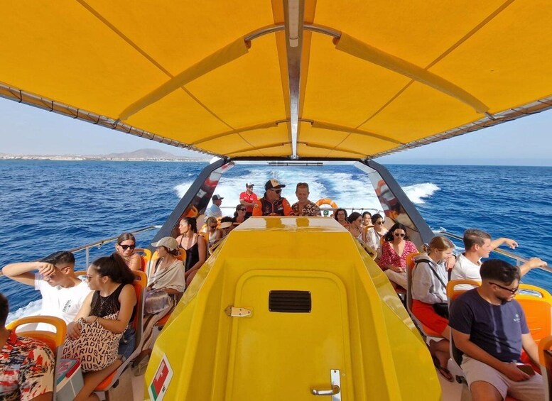 A yellow boat with passengers on a sunny day, heading towards a coastline with buildings in the distance. 3