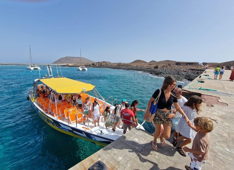 A boat with passengers boarding at a dock, a rocky shoreline, and a clear blue sea. 2
