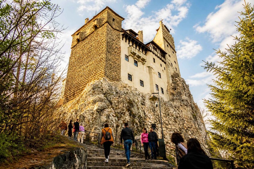 A castle on a rocky hill with people walking up the stairs. 4