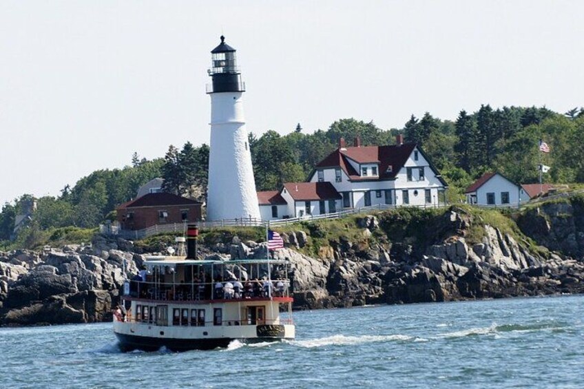 Un bateau blanc transportant des passagers, un phare et des maisons sur une côte rocheuse. 1
