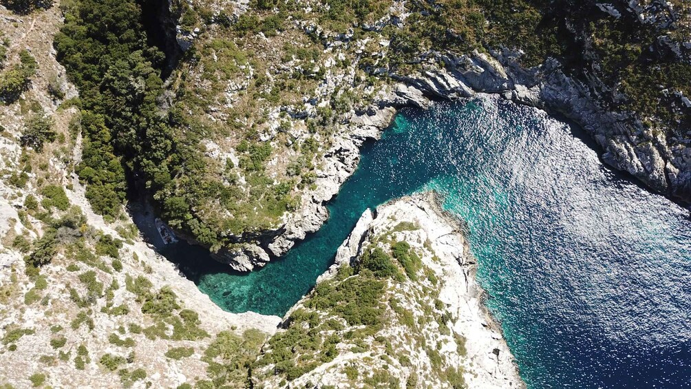 A coastal landscape with rocky cliffs, clear turquoise waters, and sparse vegetation. 3