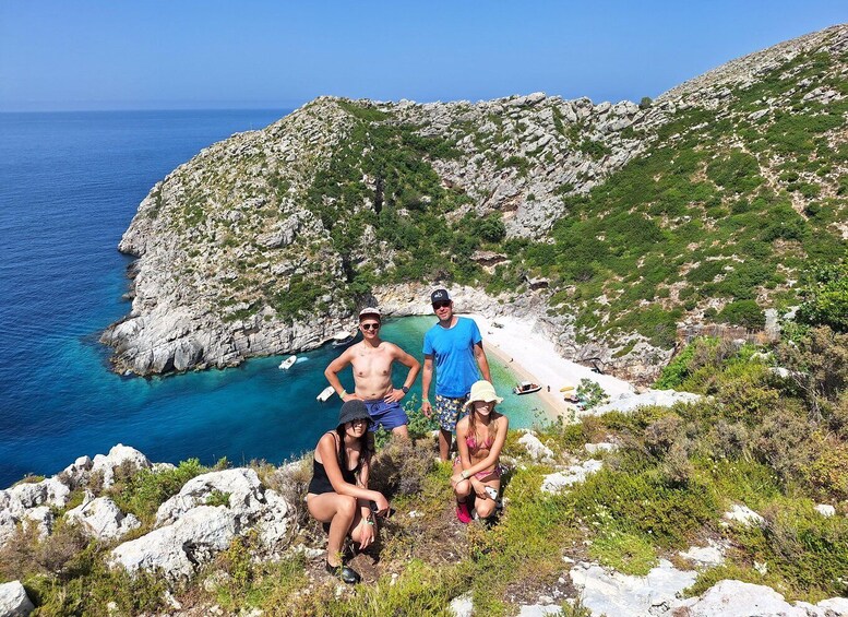 A group of people on a rocky cliff overlooking a beach with clear blue water. 1
