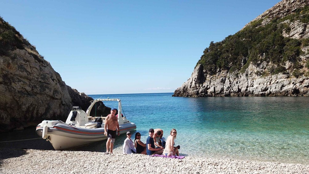 A group of people on a pebbled beach with a boat docked nearby. 4
