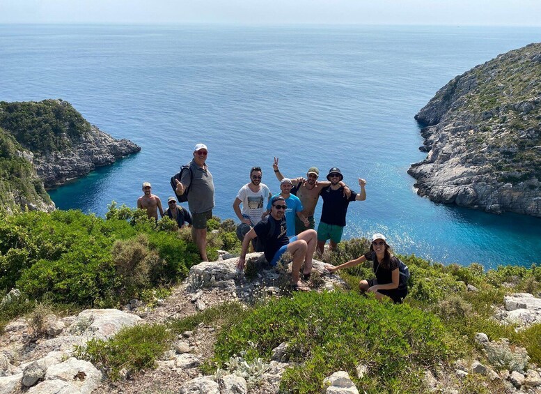 A group of people on a rocky hillside overlooking a coastal area with clear blue waters and rocky cliffs. 5