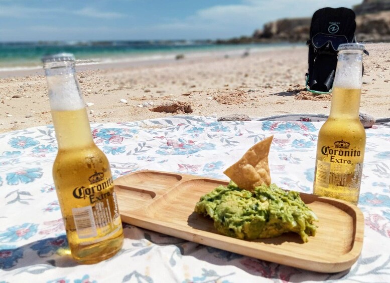 Zwei Flaschen Corona Extra Bier, ein Serviertablett mit Guacamole und ein Schnorchel am Strand. 2