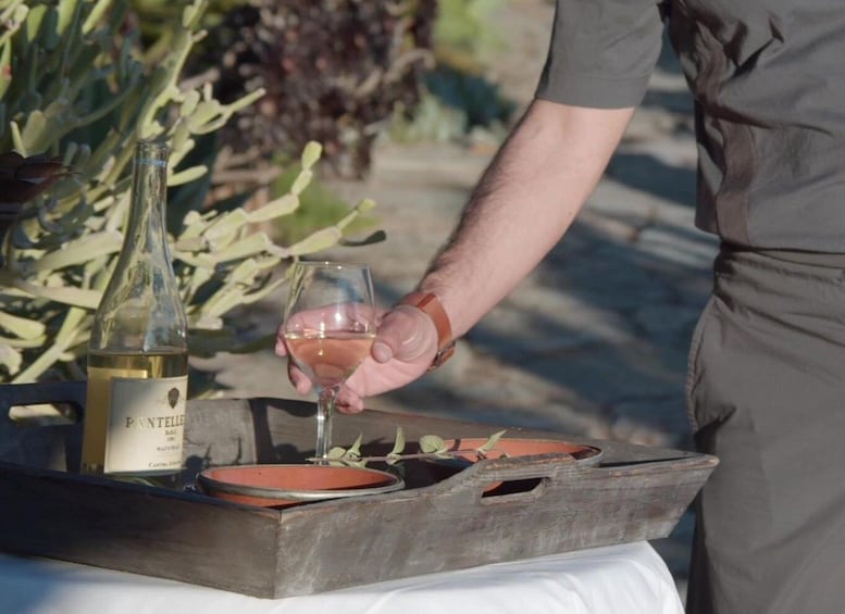 A person pouring wine into a glass from a bottle labeled 'PANTHELEON' on a wooden tray with plates. 2