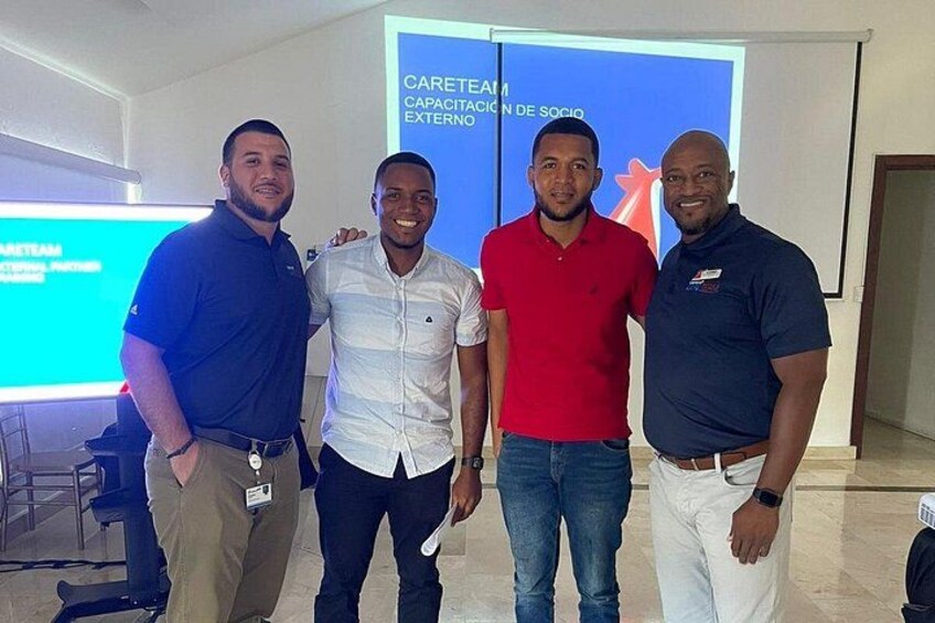 Four men standing in a room with a presentation screen in the background. 3