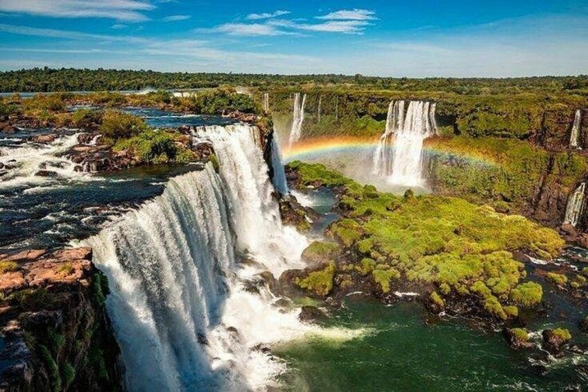 Una cascada con un arcoíris, abundante vegetación y un río. 1