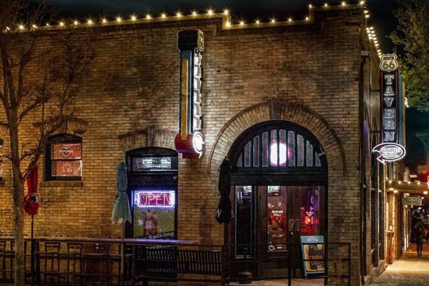 A brick building with a neon sign, a vintage telephone booth, and a sign for a Route 66 tavern. 3