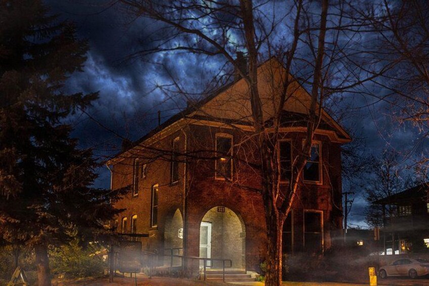 A brick house with a large arched entrance, surrounded by trees and a cloudy sky. 5