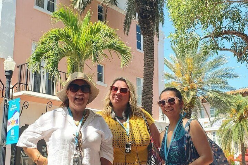 Three people standing outdoors with palm trees and a building in the background. 3