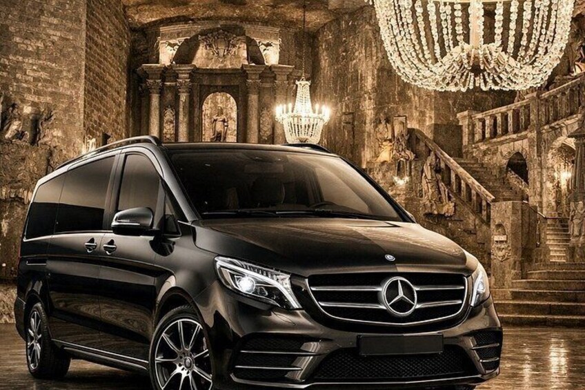 Een zwarte Mercedes-Benz SUV voor een versierd historisch gebouw met stenen bogen en kroonluchters. 4