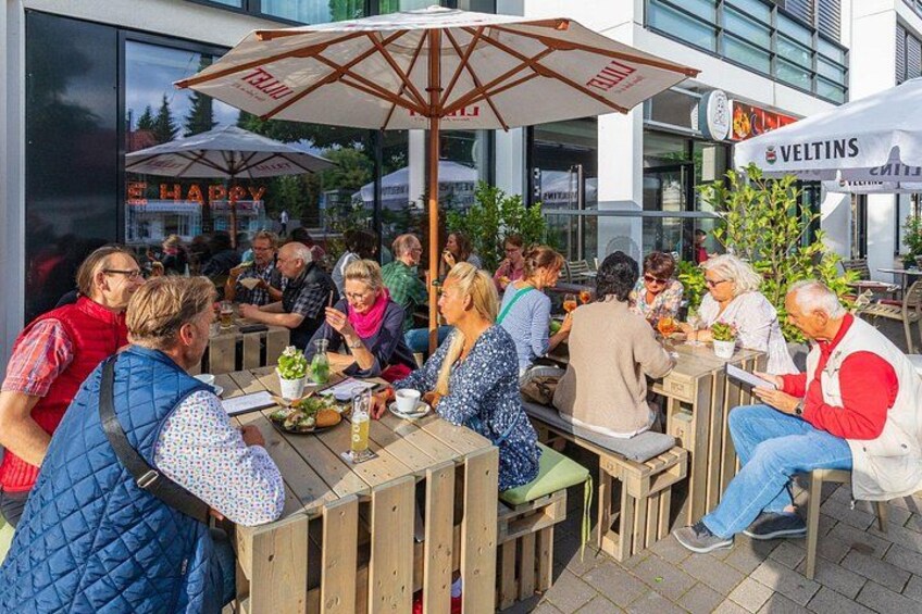 Persone che cenano all'aperto in un ristorante con tavoli di legno e ombrelloni. 2