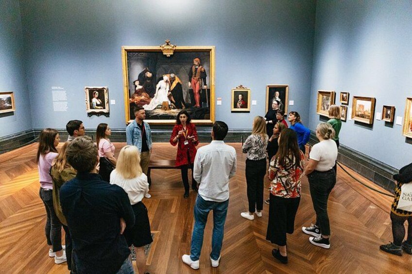 En grupp människor i ett museum, samlade framför en stor målning. 2