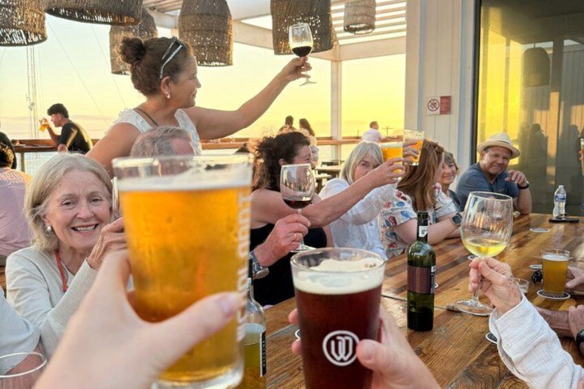 People toasting with beer glasses at a wooden table with a view of the sea. 1