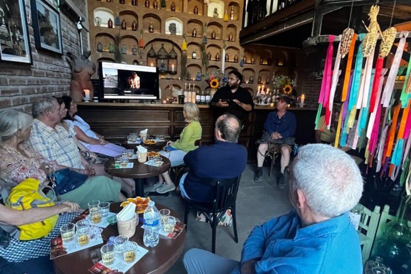 A group of people seated around a table with a television, in a room with brick walls and decorative items. 5