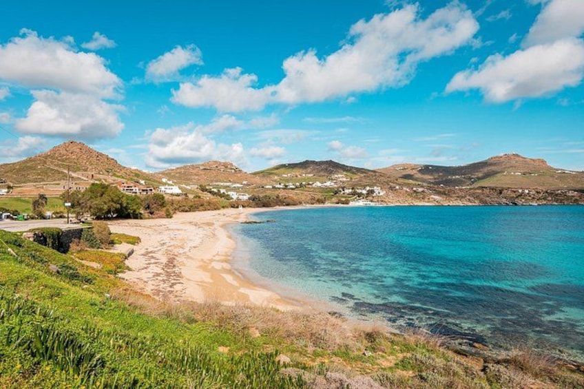 A coastal landscape with clear blue waters, sandy beach, and rolling hills in the background. 3