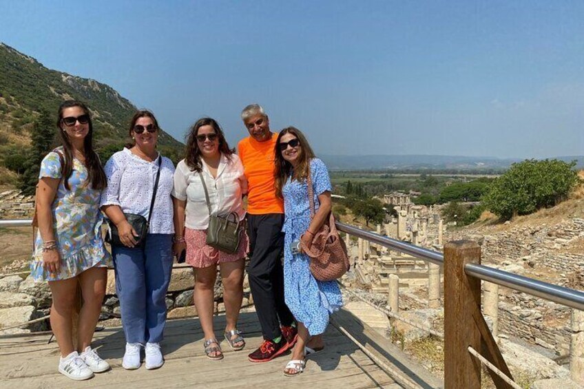A group of people standing on a wooden boardwalk with a view of ancient ruins and a hilly landscape in the background. 4