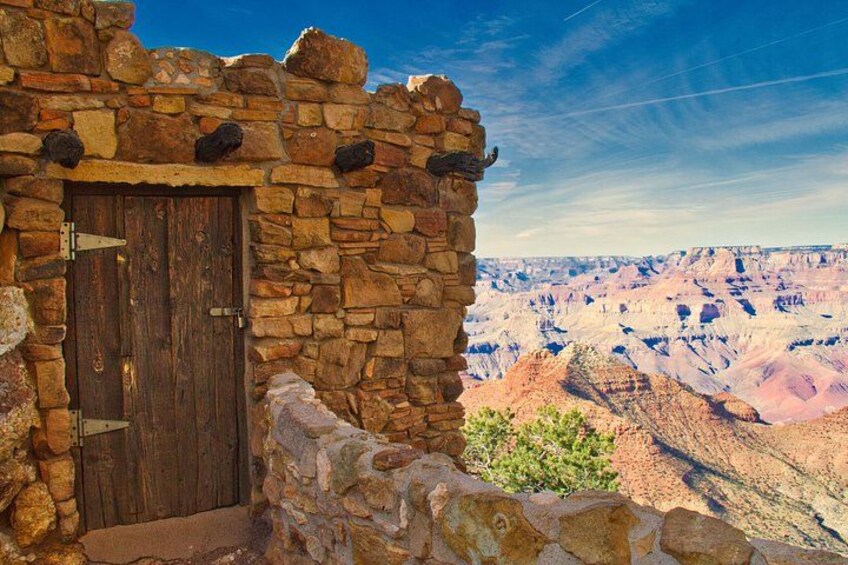 A stone building with a wooden door, overlooking a canyon with layered rock formations. 3