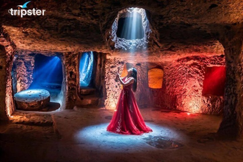 A person in a red dress in a cave-like setting with a stone structure and a blue light source. 2