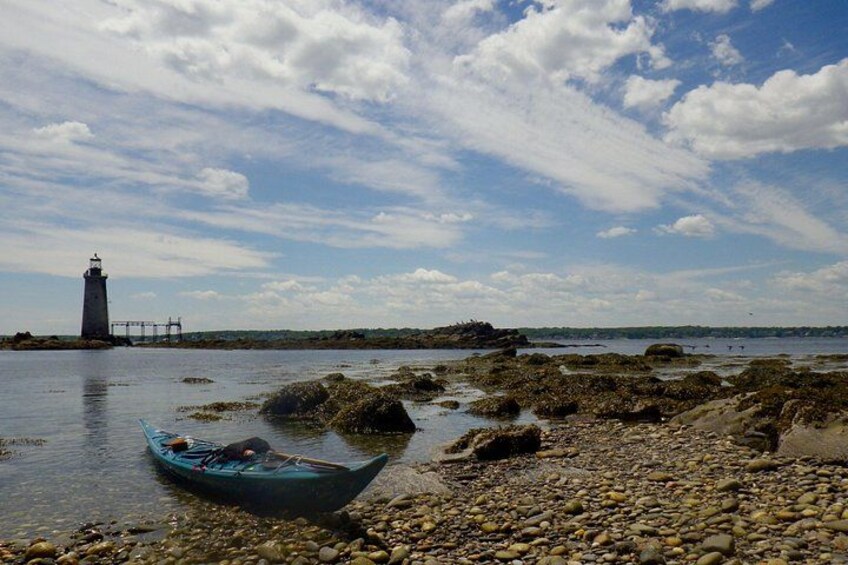 A rocky shoreline with a lighthouse in the distance and a small boat on the water. 4