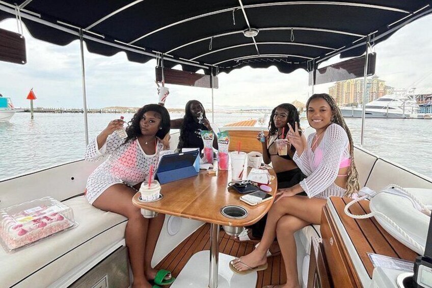 Un grupo de personas en un bote con una mesa, bebidas y un paisaje urbano de fondo. 5