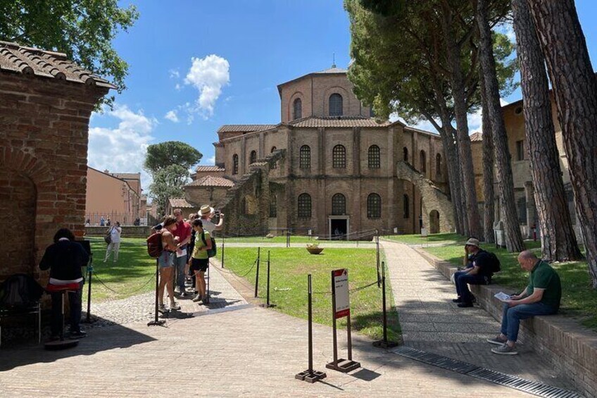 A historic building with tourists, a paved pathway, and trees. 5