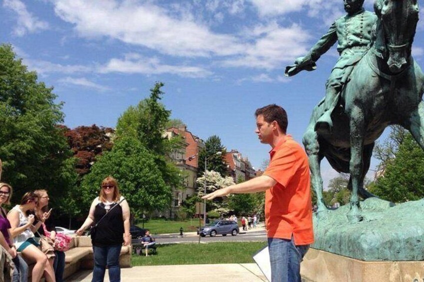 En statue af en person til hest i en park med folk omkring. 4