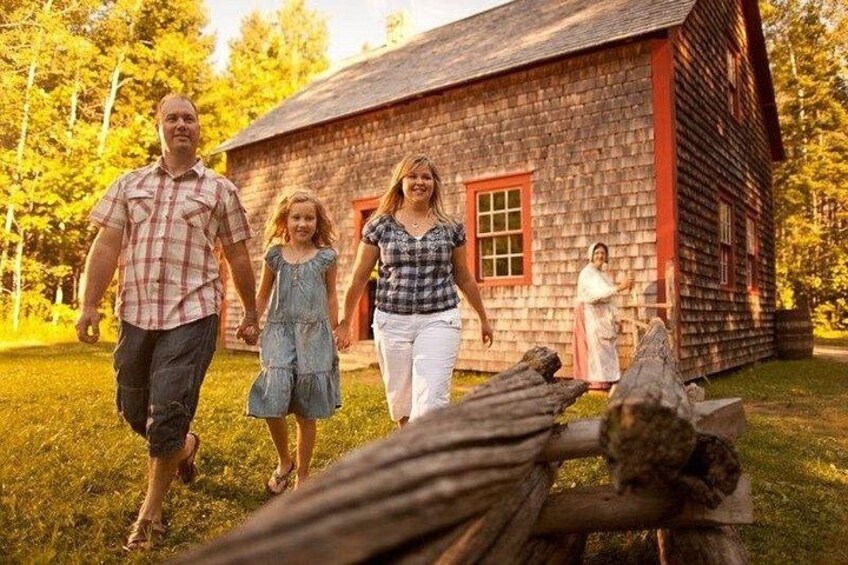 A family walking towards a log cabin with a red door and a woman in traditional attire standing by the door. 1