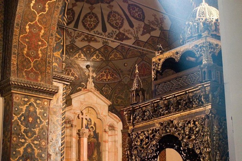 An ornate interior with detailed ceiling artwork, a central statue, and elaborate wall carvings. 5