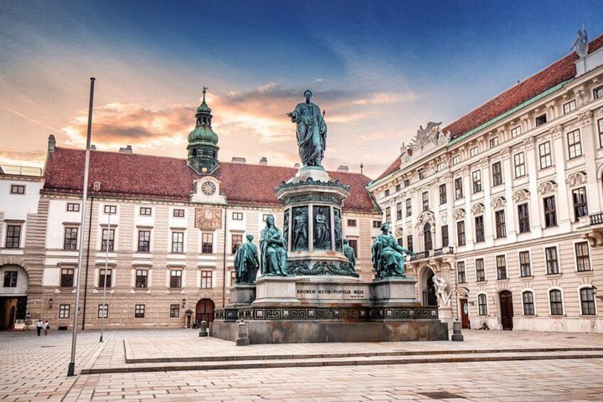 A historical square with a central statue, buildings with classical architecture, and a clock tower. 4